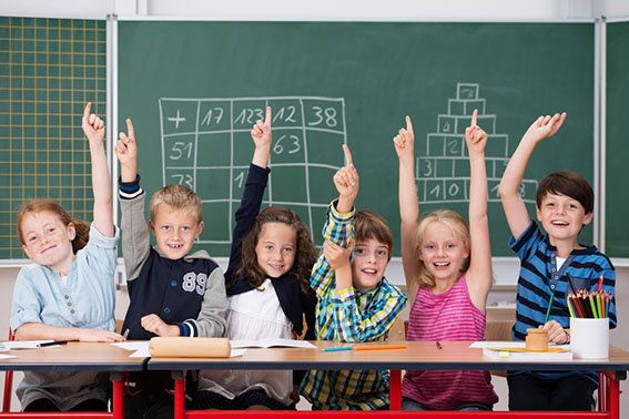 Enthusiastic group of young kids in class sitting in a row at their desk raising their hands in the air to show the know the answer to a question Enthusiastic group of young kids in class sitting in a row at their desk raising their hands in the air to show the know the answer to a question